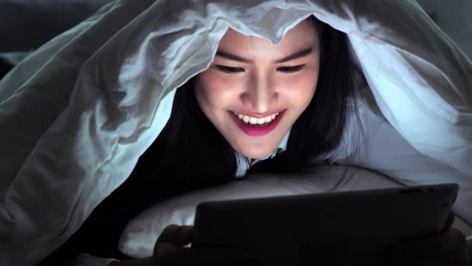 年轻女性在毯子下使用平板电脑t night.edu阳离子，技术，创新，科学和人的概念