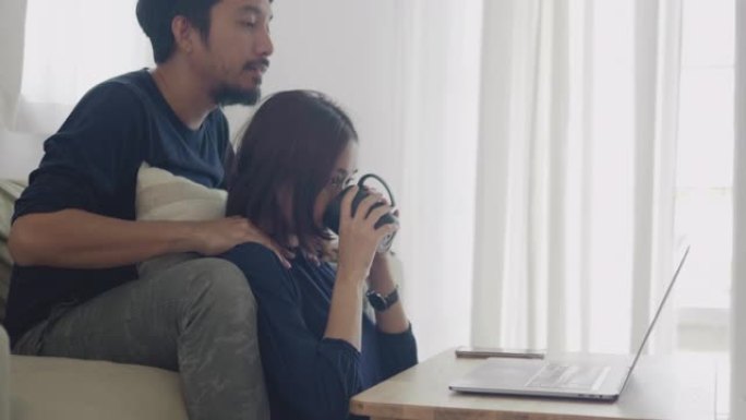 亚洲夫妇在家沙发上用笔记本电脑工作。