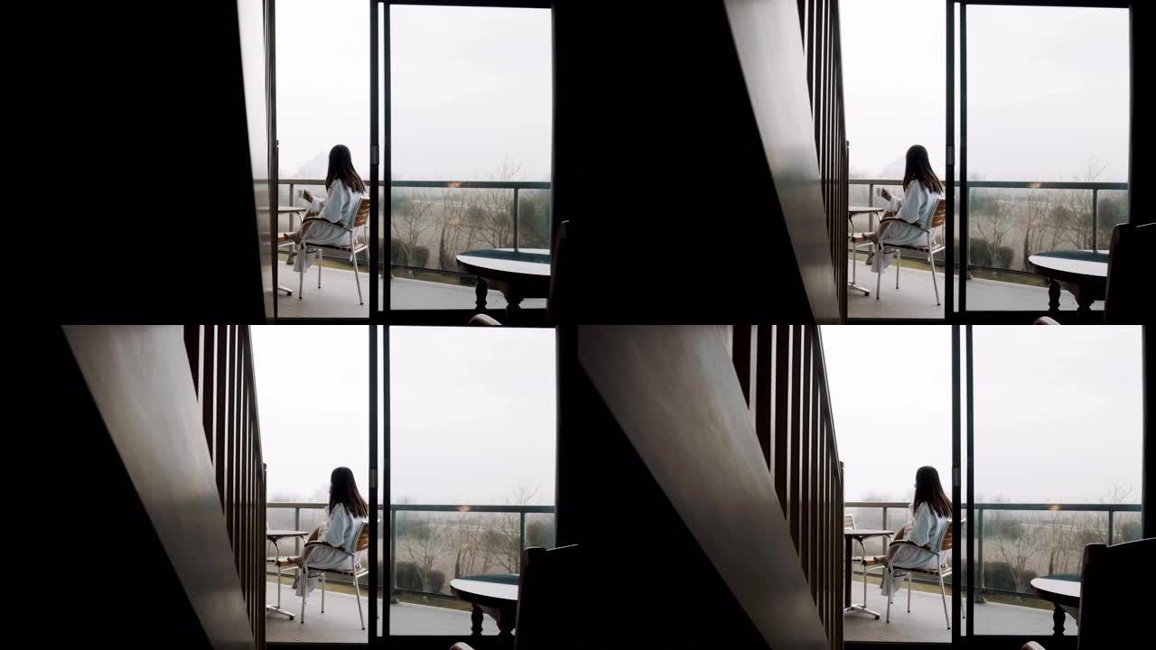 镜头向右滑动，揭示了穿着礼服的漂亮女人在房间露台上喝咖啡，秋天有雾。