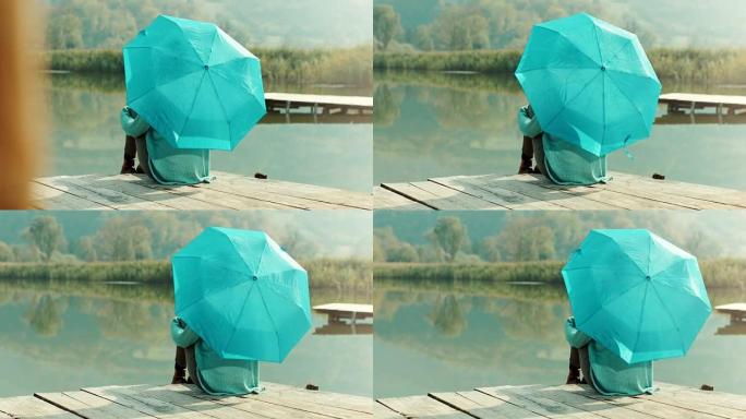 坐在湖边码头上的蓝色雨伞的女人