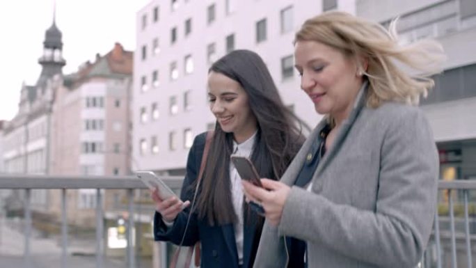 年轻的女商人女士与智能手机的朋友沿着城市桥梁行走