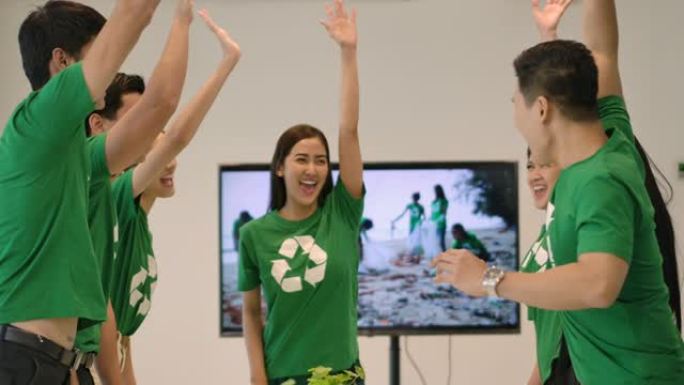 4k志愿者团队开会。一群穿着绿色t恤的亚洲年轻人志愿者在现代办公室里团结一致，团队合作。