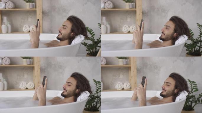 躺在浴缸里使用智能手机的快乐男人