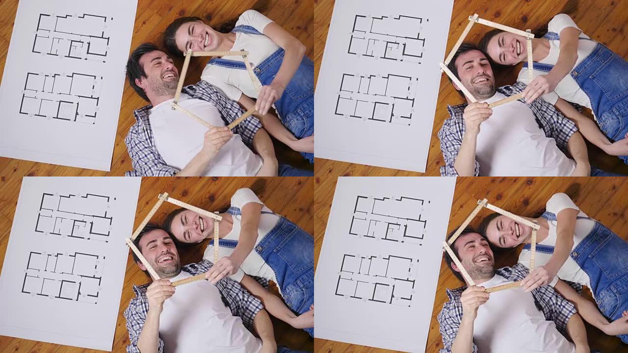 一对相爱的夫妇躺在地上，谁想买新房子的俯视图，他们带着想象力旅行，他们将如何在未来和梦想一个新房子。