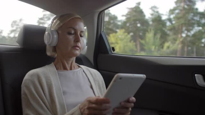 乘坐汽车时戴耳机使用平板电脑的女人