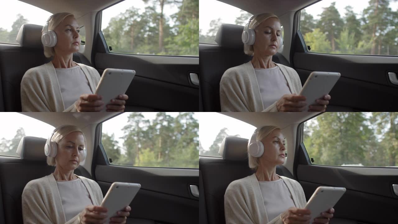 乘坐汽车时戴耳机使用平板电脑的女人