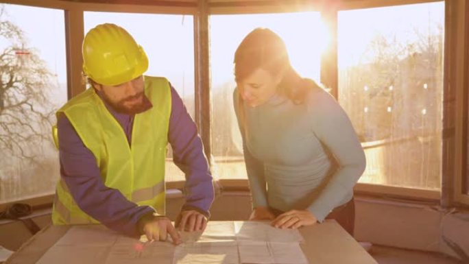 特写: 年轻女子和承包商在金色日落时讨论平面图。