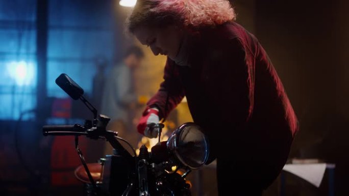 年轻漂亮的女机械师正在修理一辆定制的摩托车。穿着方格衬衫的天才女孩。她用棘轮扳手。创意正宗车间车库。
