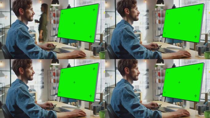 留着胡须和牛仔裤衬衫的男性创意设计师在他的个人计算机上工作，并带有绿色大屏幕模拟显示。他在一个很酷的