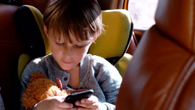 快乐兴奋的小4-6岁高加索男孩微笑，使用智能手机坐在汽车儿童安全座椅上的玩具。