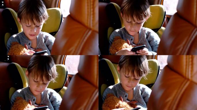 快乐兴奋的小4-6岁高加索男孩微笑，使用智能手机坐在汽车儿童安全座椅上的玩具。