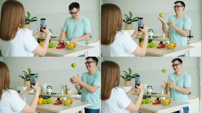 当女孩用智能手机录制视频时，男人煮沙拉然后杂耍苹果