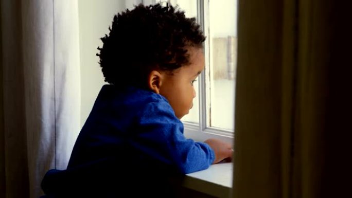 舒适的家庭4k中，可爱的小黑男孩靠在窗台上的侧视图