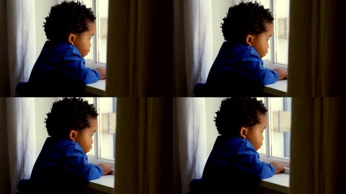 舒适的家庭4k中，可爱的小黑男孩靠在窗台上的侧视图