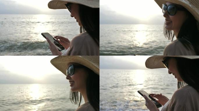 亚洲妇女使用手机并在海滩上看智能手机