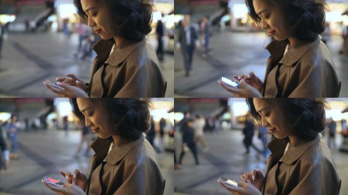 漂亮年轻的亚洲女人晚上在城市街道上使用手机，4k