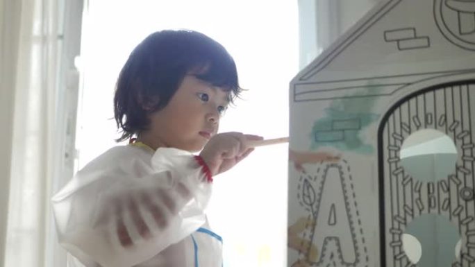 亚洲儿童在家建造和绘画玩具纸板屋。
