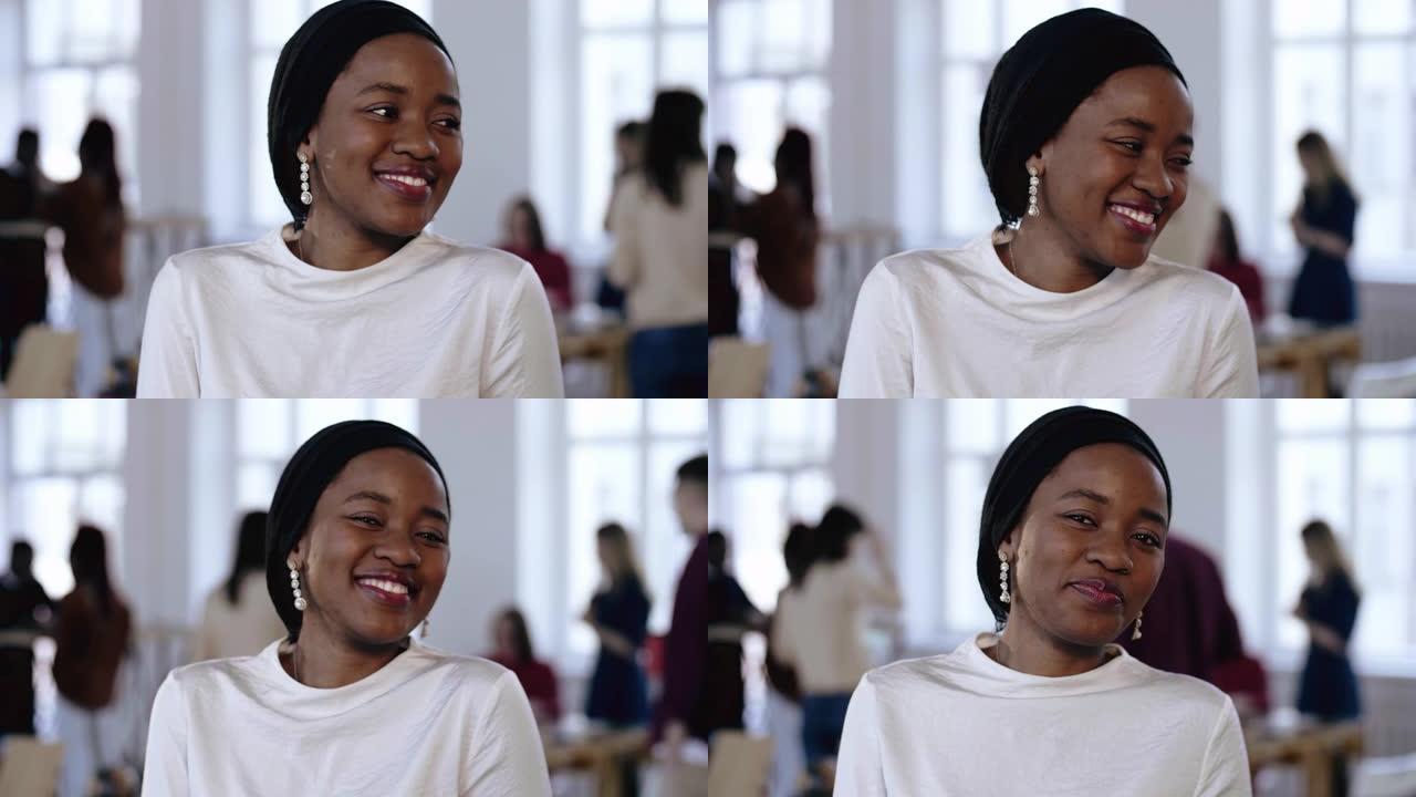 年轻的职业成功的非洲女企业家戴着种族头巾，在现代办公室谦逊地微笑。