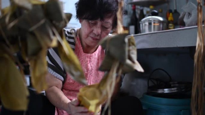 一位亚洲华裔高级妇女在厨房里准备zong子中国饺子，并将其包裹起来，为端午节做准备