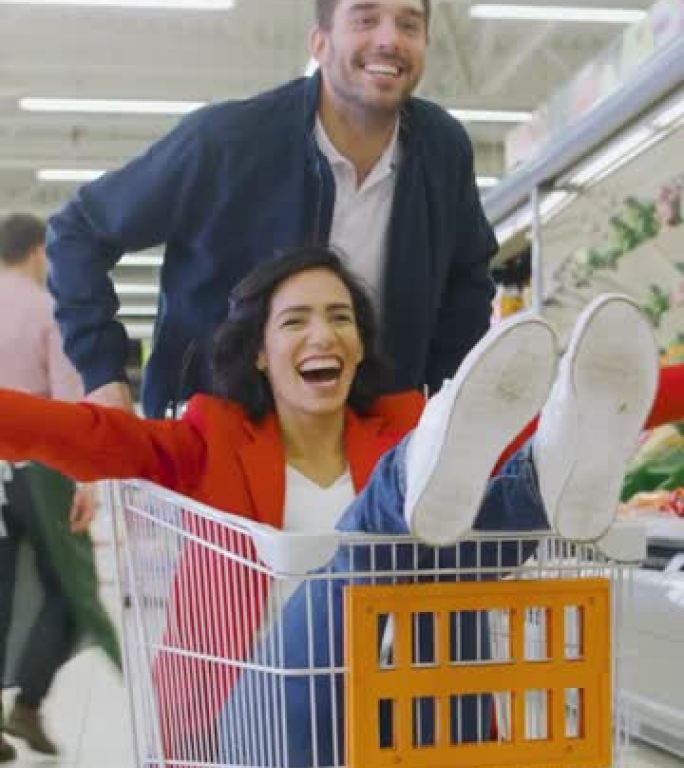 在超市: 男人推着购物车，女人坐在里面。幸福的夫妇在手推车上穿过商店时玩得很开心。垂直屏幕方向视频9