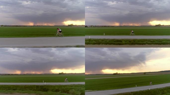 WS男骑自行车者在乡村道路上骑自行车，背景为暴风云和闪电