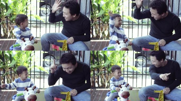 亚洲单身爸爸带着儿子在现代房子前草坪上玩玩具车的4k慢动作镜头，用于自学或家庭学校，家庭和童年的概念