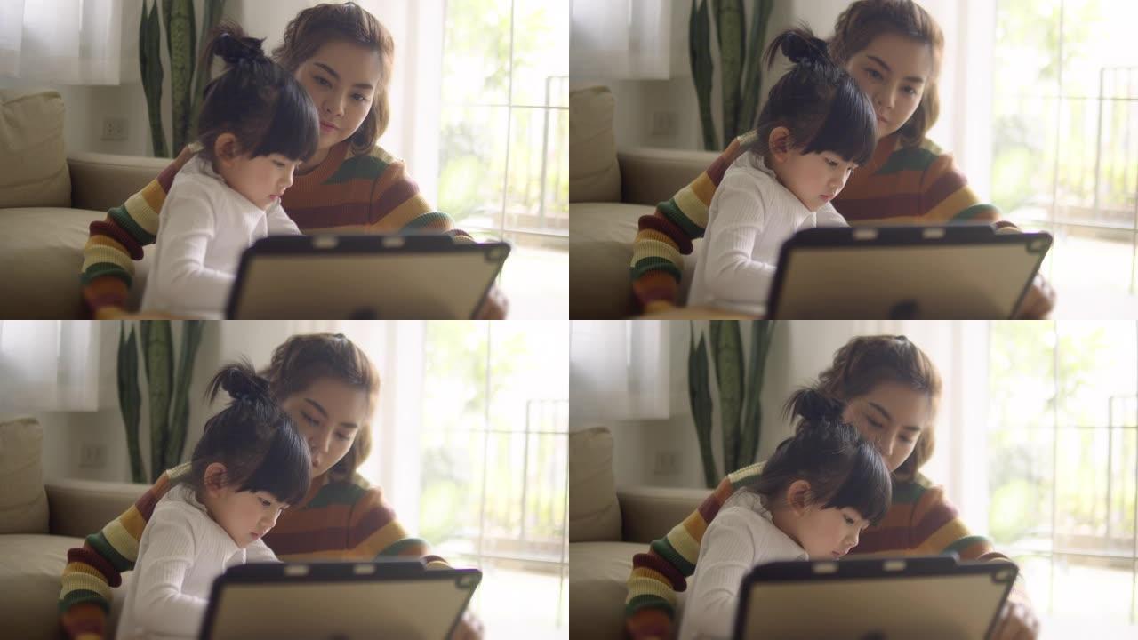 年轻的母亲带着女儿在家用数字平板电脑做作业。