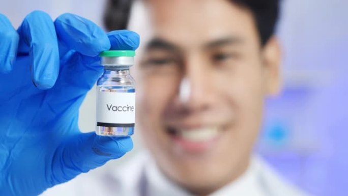 领导亚洲男性科学家微笑着，手拿安瓿在科学实验室的病毒研究冠状病毒或Covid-19疫苗。在生命科学实