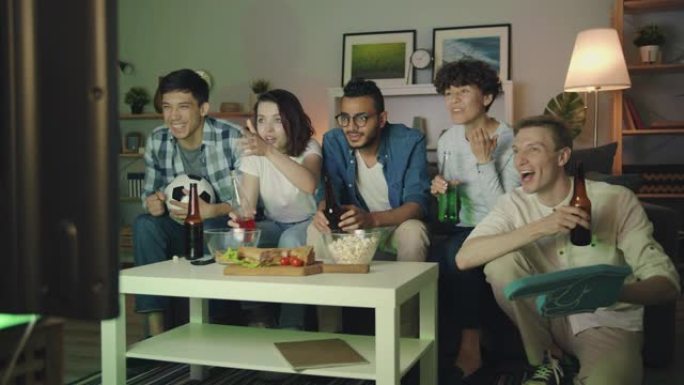 一群朋友在晚上在电视上看足球，叮叮当当的瓶子玩得开心