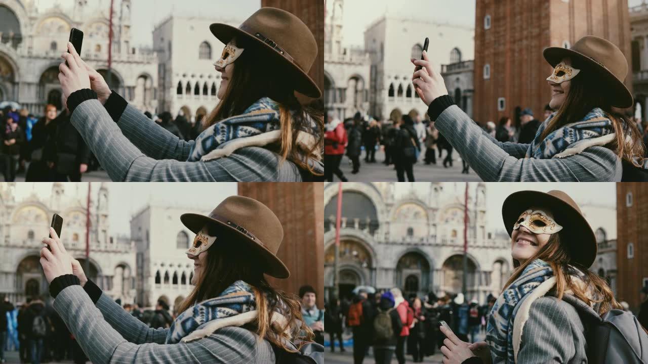 戴着时尚帽子和白色狂欢节面罩的幸福女人在意大利威尼斯城市广场微笑着自拍。