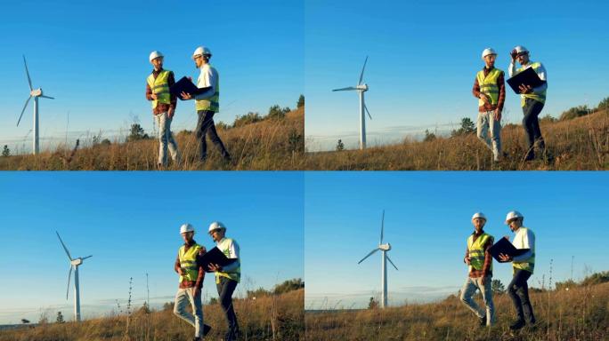 一个由两名能量学专家走过的领域和一个运转正常的涡轮机塔。清洁、环保的能源概念。