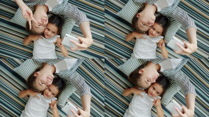 女孩和母亲用智能手机躺在地板上自拍，做鬼脸