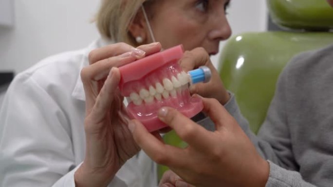女牙医的特写，向年轻的男性患者展示如何正确刷牙