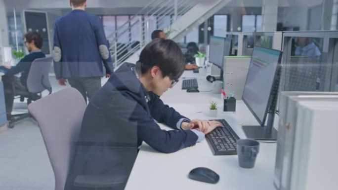 年轻的日本经理在台式电脑的工作场所很累，睡着了。在现代开放式办公室中，多元化的多民族商人在计算机上工