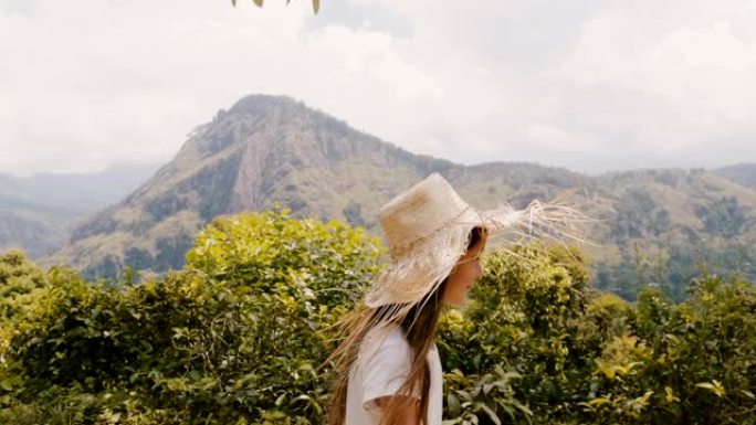 侧视跟踪拍摄快乐的小女孩戴着大草帽沿着美丽的阳光明媚的森林山路散步。