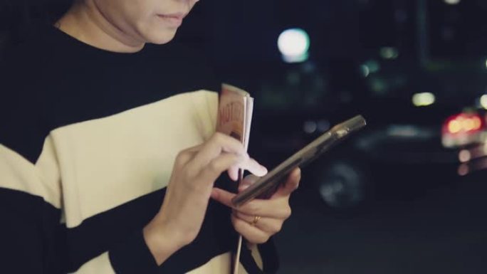 亚洲女性晚上在城市街道上用智能手机发短信。