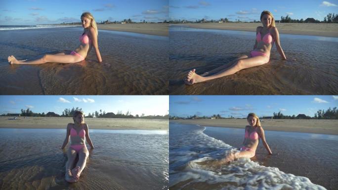 南非，一个微笑着的美丽年轻女子坐在海滩上的浅水里的4k慢动作视图