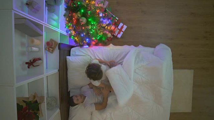 这对幸福的夫妻在圣诞树附近的床上玩耍。晚上时间