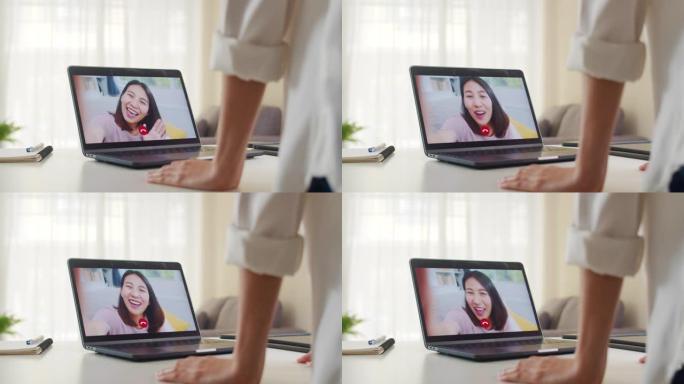 年轻的亚洲商界女性在客厅在家工作时使用笔记本电脑视频通话与朋友交谈。