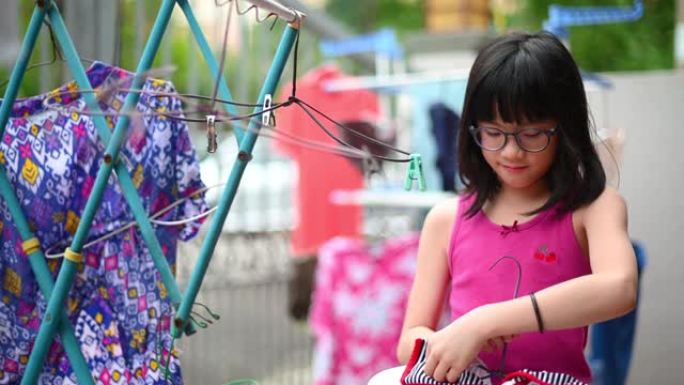 一个顽皮的年轻亚洲华裔女孩在阳光下晾干衣服，帮助她的父母在房子的前院