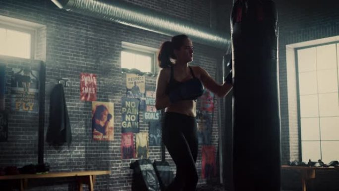美丽健康的黑发跆拳道站在阁楼健身房，配有激励海报。她屏住呼吸，继续进行激烈的自卫训练。运动员脸上和身