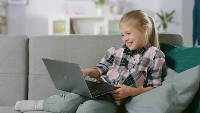 可爱的小女孩躺在沙发上，使用笔记本电脑，观看有趣的视频和卡通。