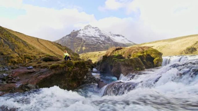 女士坐在俯瞰冰岛瀑布的岩石上