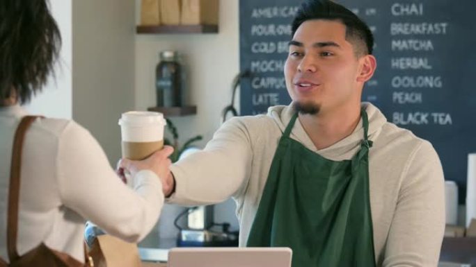 一位男咖啡师微笑着与她交谈时，递给顾客咖啡。
