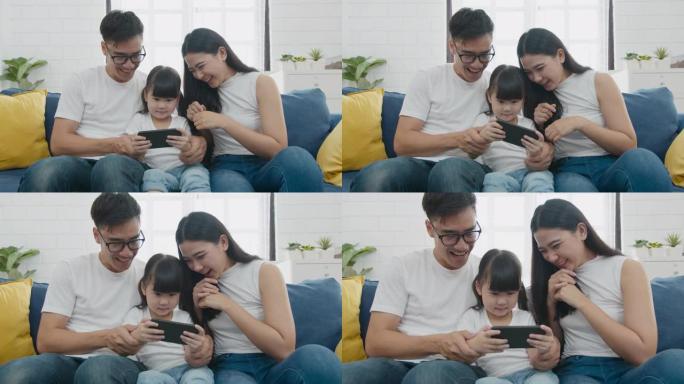 慢动作缩放镜头: 快乐温暖的家庭父亲，母亲和女儿在智能手机上在线玩有趣的游戏，一起坐在沙发上，父母带