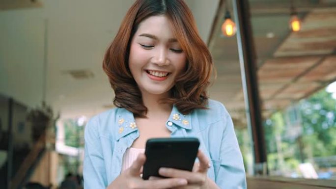快乐快乐的亚洲年轻女子坐在咖啡馆里，用智能手机聊天、阅读和发短信。女性生活方式概念。