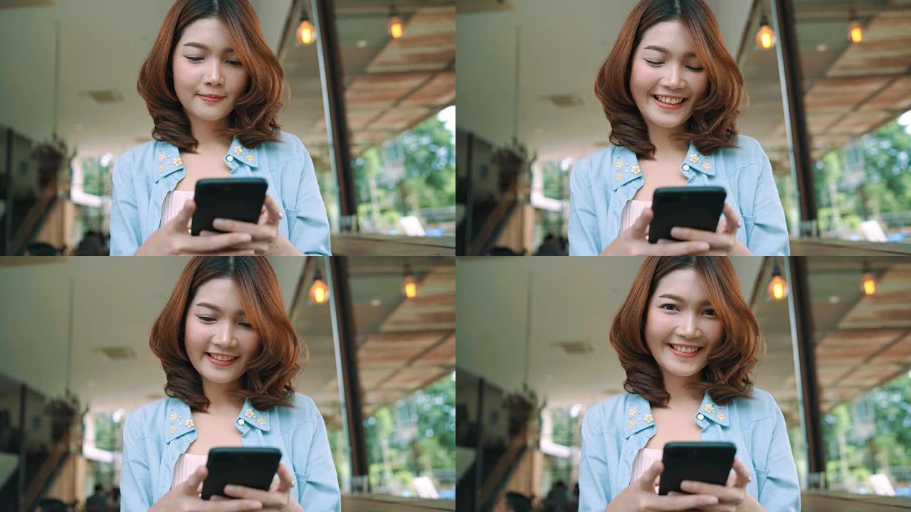 快乐快乐的亚洲年轻女子坐在咖啡馆里，用智能手机聊天、阅读和发短信。女性生活方式概念。