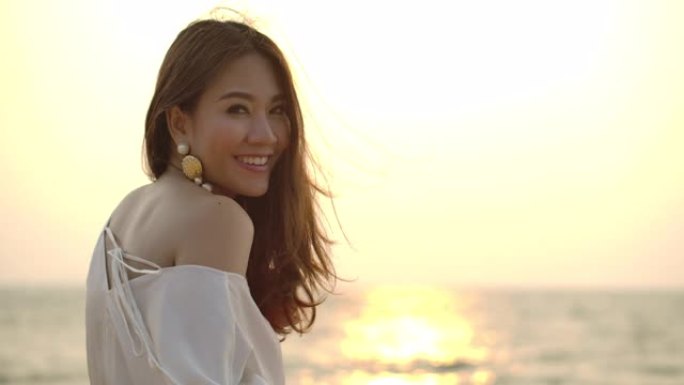 年轻迷人的亚洲女性享受生活方式的肖像，看着海滩日落背景的相机。健康开朗的女士，美丽的脸庞肖像。女性美
