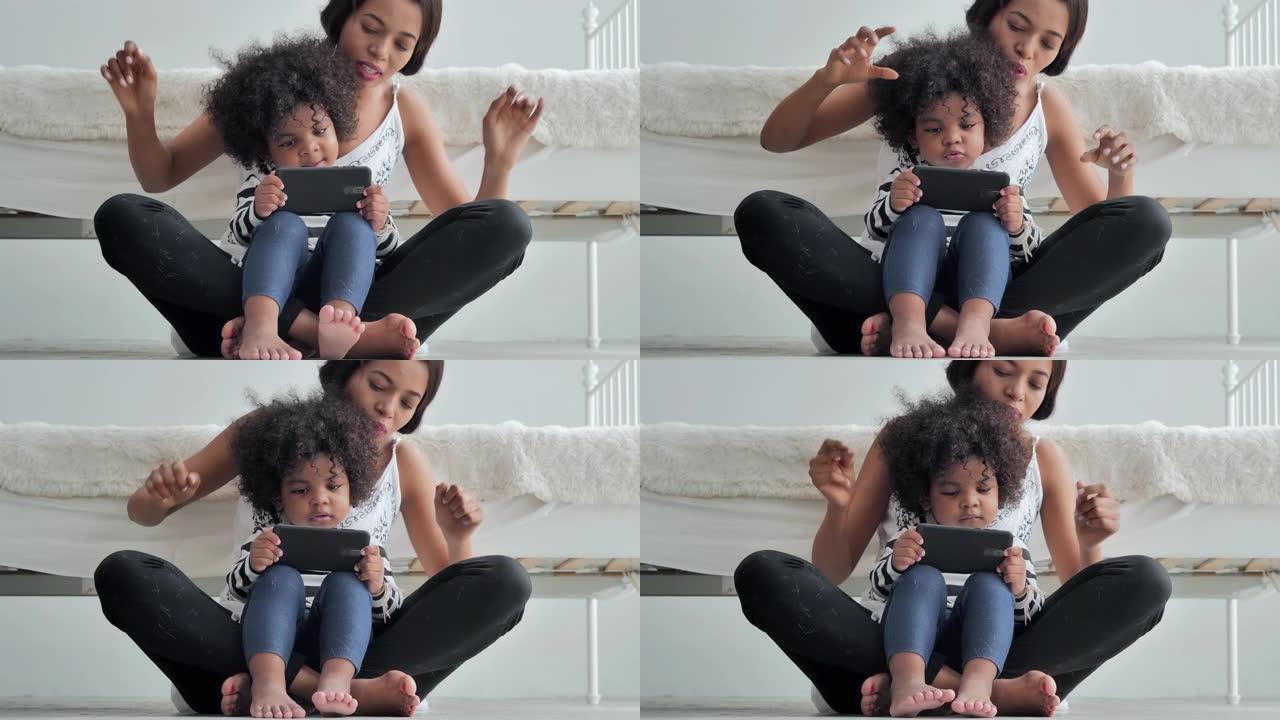快乐的非洲裔美国母亲和孩子使用智能手机观看，唱歌卡通玩得开心。花时间和她可爱的男婴在家里。家庭、生活