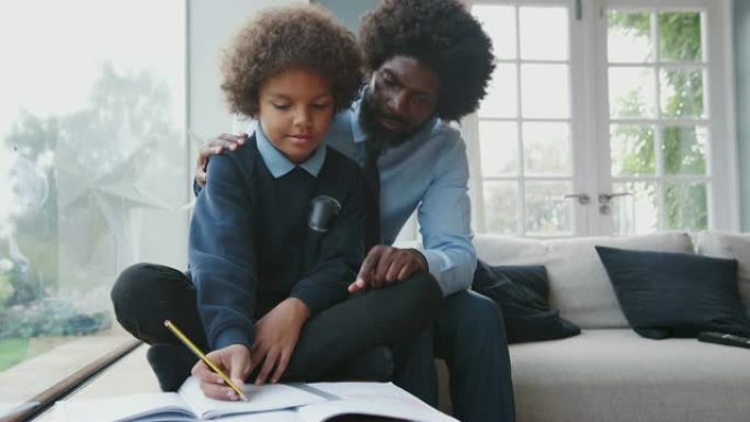 中年黑人父亲坐在他的儿子后面，在家里的客厅里帮助他十几岁的儿子做作业，前视图，特写镜头